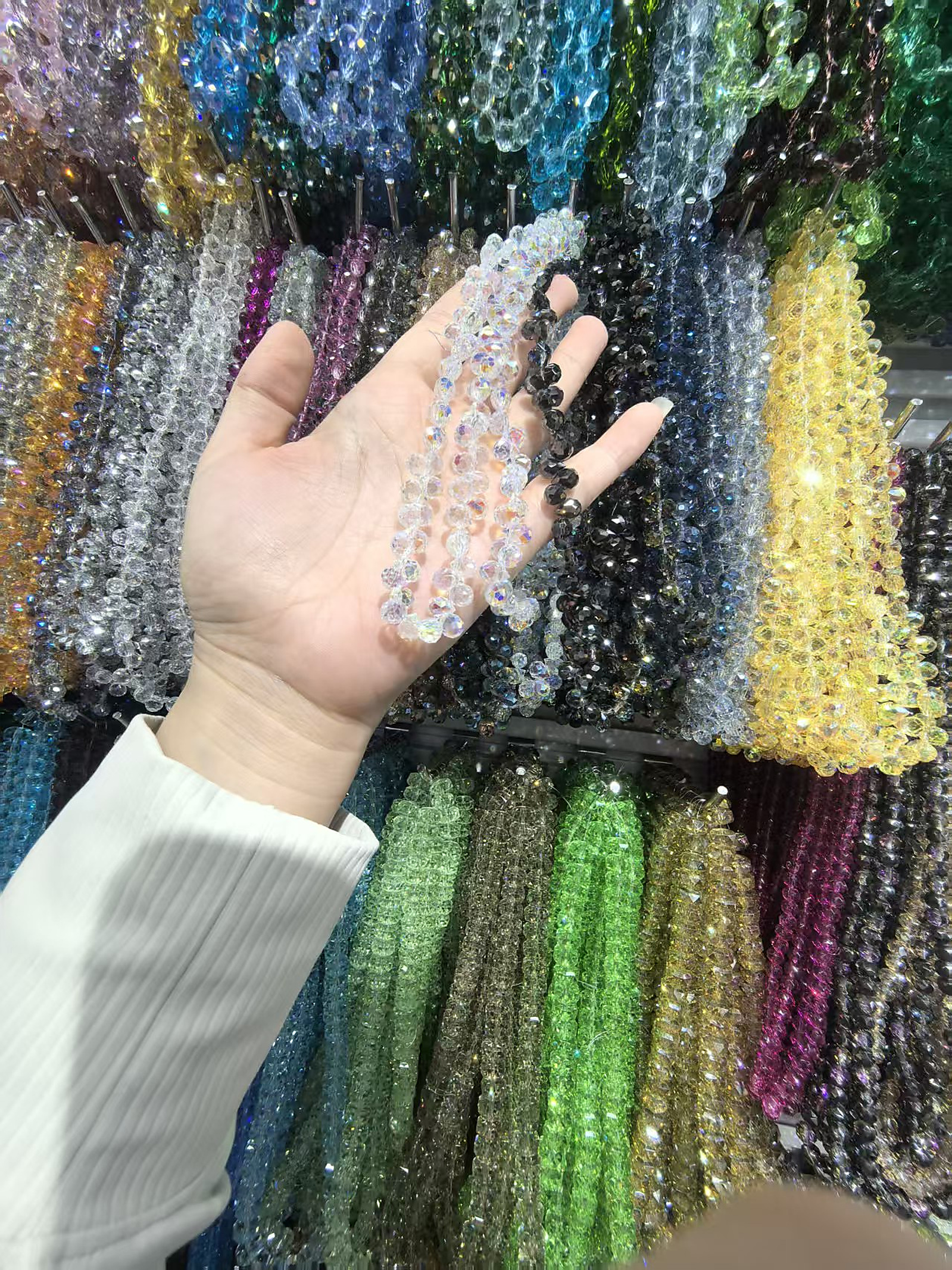 Hand comparing clear iridescent and black faceted crystal bead strands