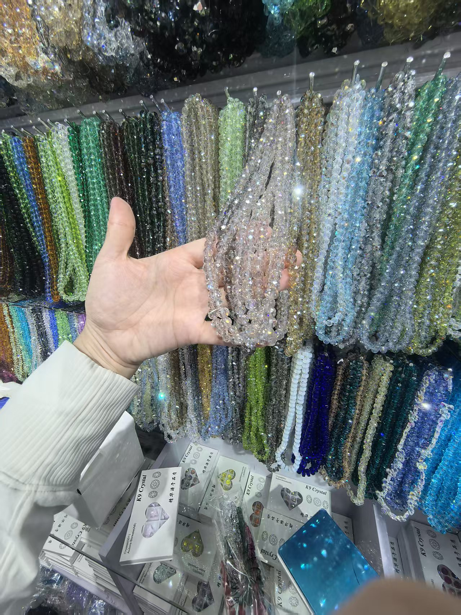 Hand holding neutral faceted crystal bead strands in a real wholesale display